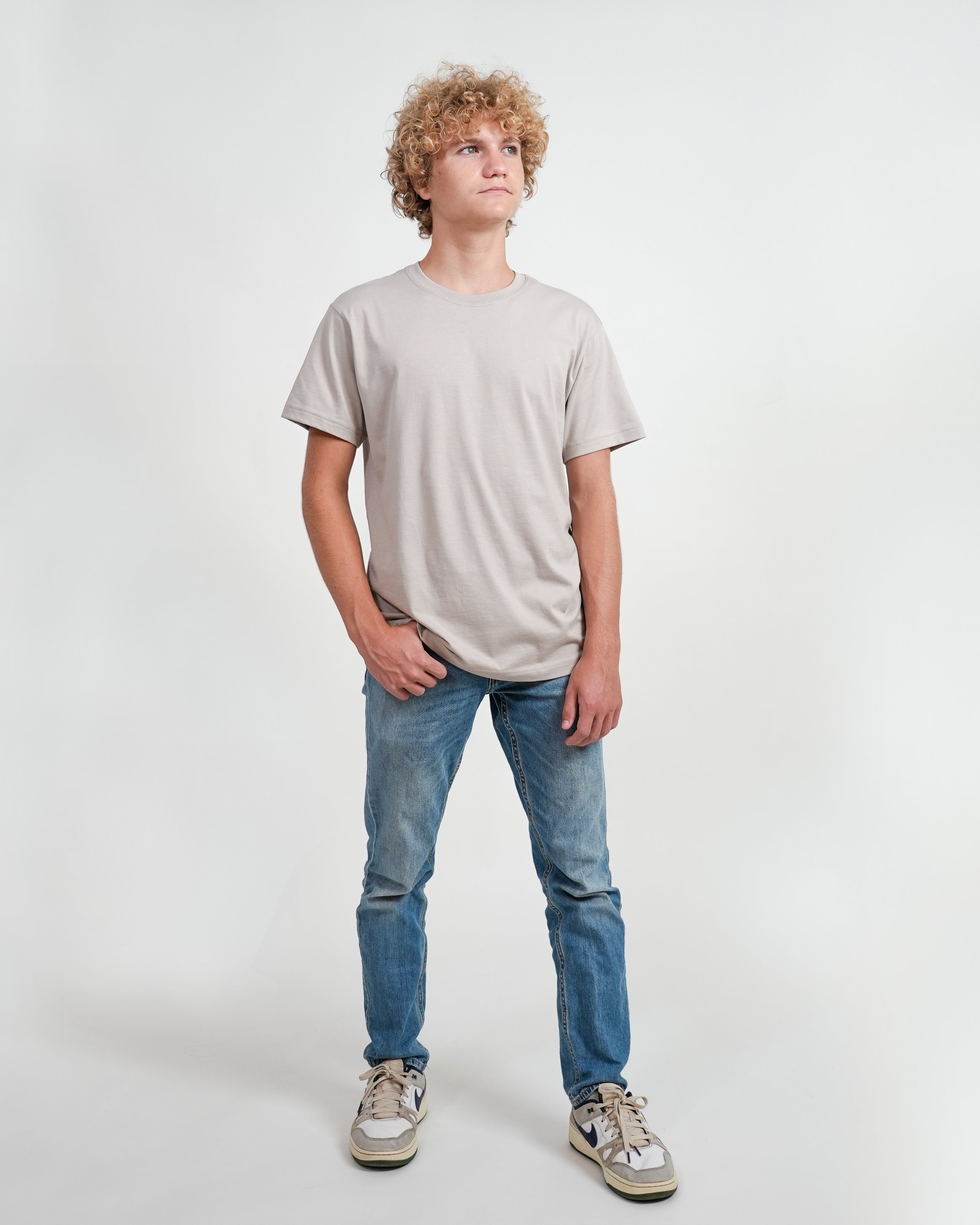 Male model wearing gray t-shirt and jeans standing against a white background.