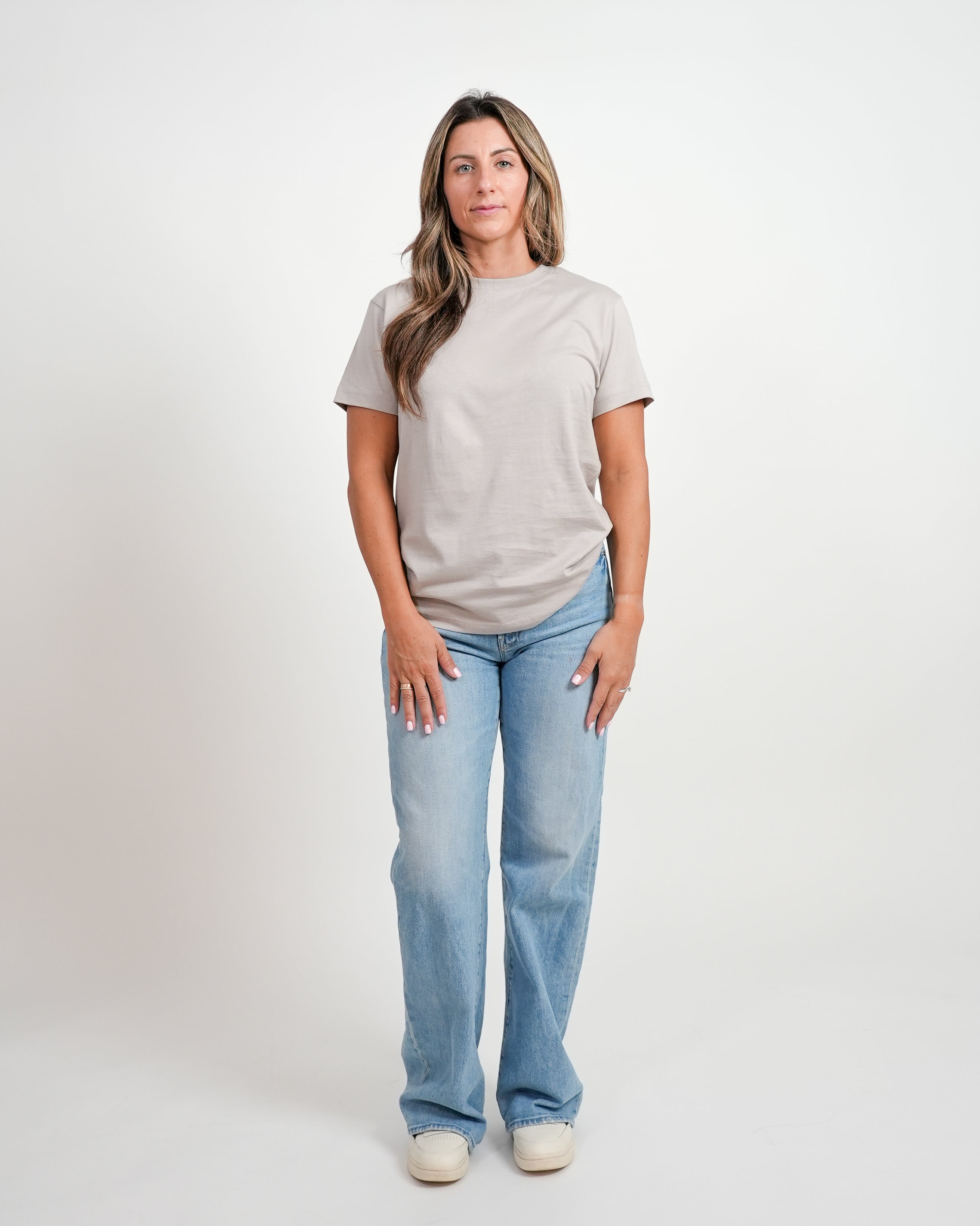 Female model wearing gray t-shirt and jeans standing against a white background.