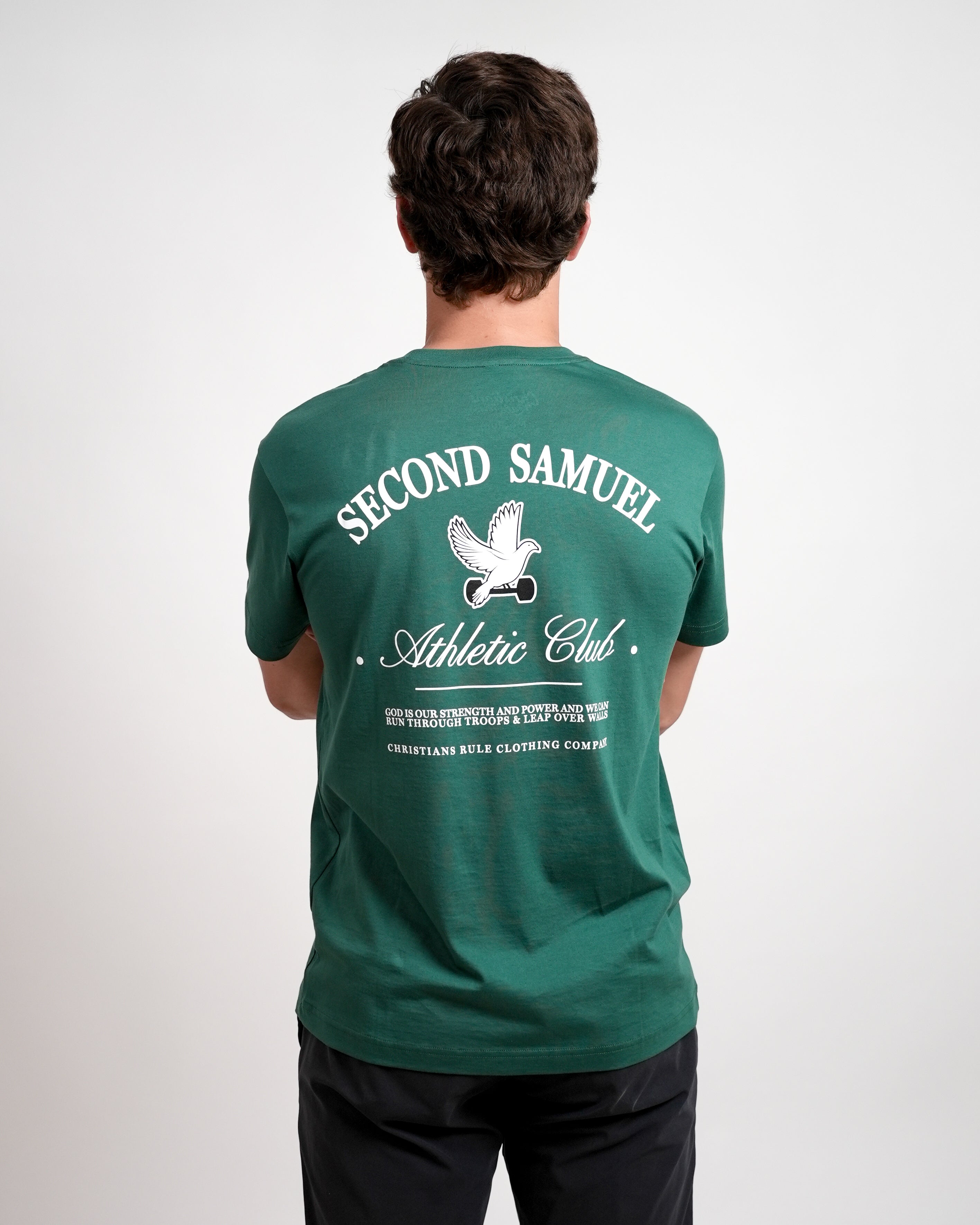 Male model wearing green Christian t-shirt with 'Second Samuel Athletic Club' text and graphic of dove holding a dumbbell; person stands against a white background.