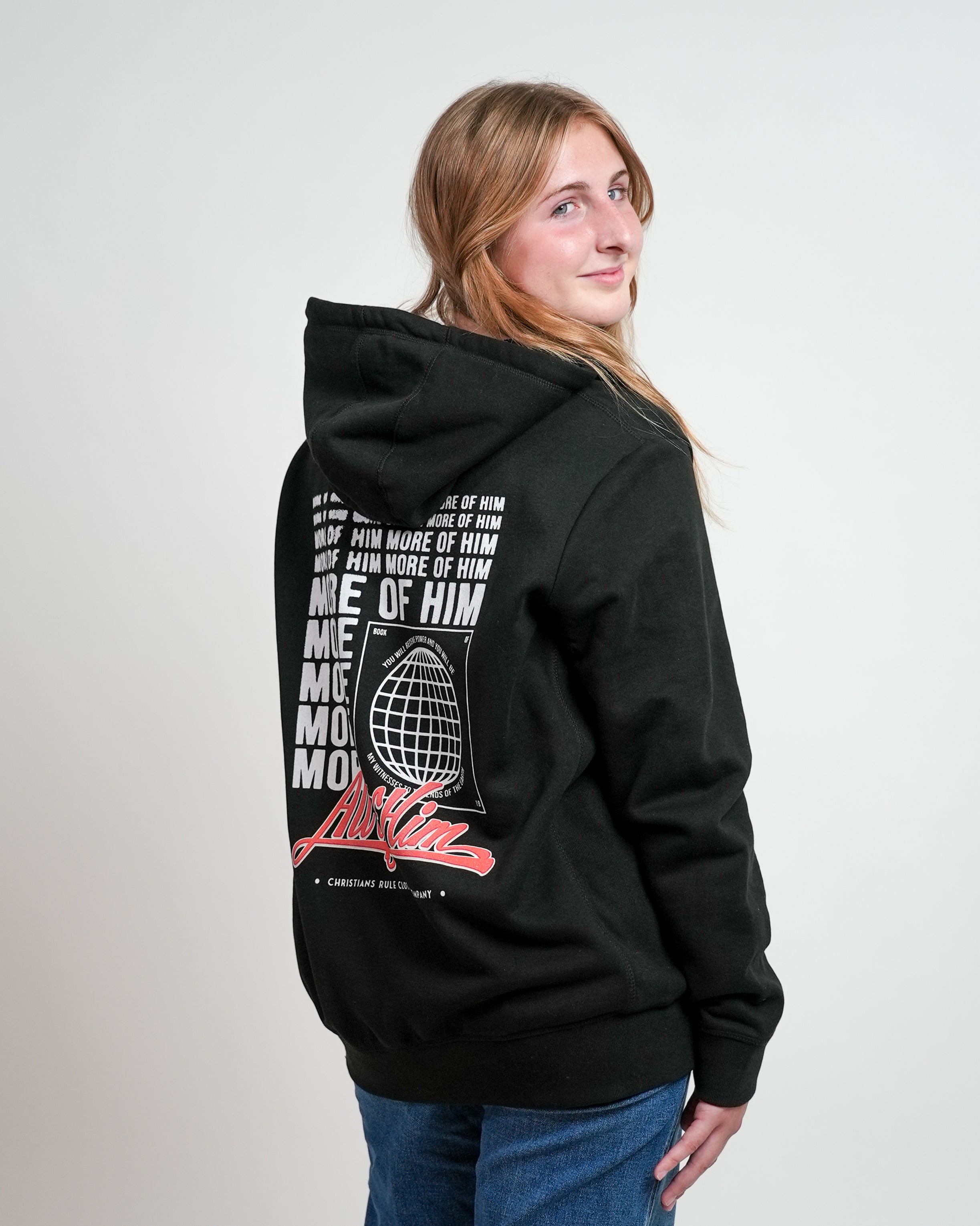 Smiling female model wearing a black Christian hoodie with stylized 'All of Him' script graphic design, standing against a white background.