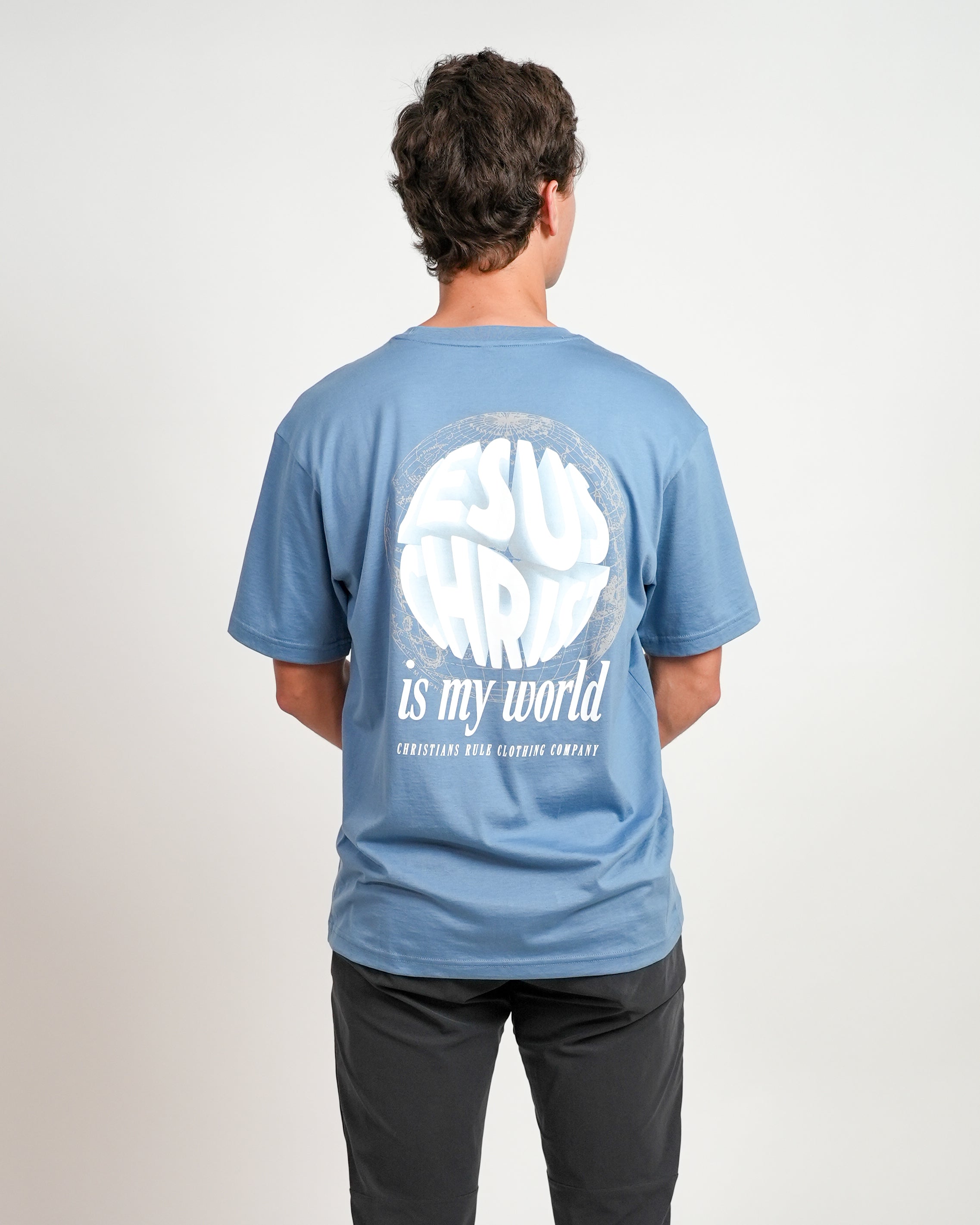 Male model wearing blue Christian t-shirt with a meridian graphic design and bold text saying "Jesus Christ is my world" and "Christians Rule Clothing Company".