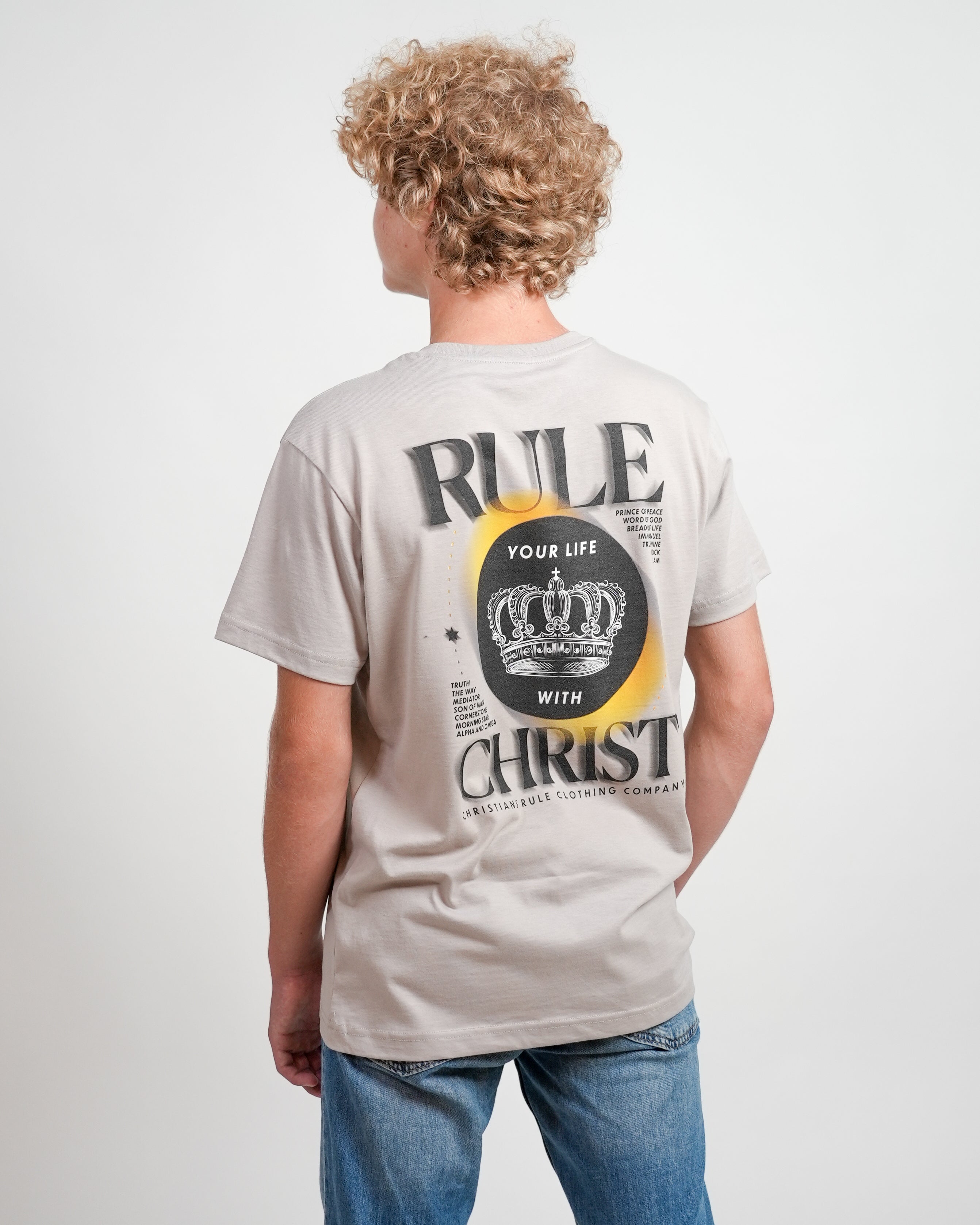 Male model wearing gray Christian t-shirt with "Rule Your Life with Christ" graphic and jeans, standing against a white background.