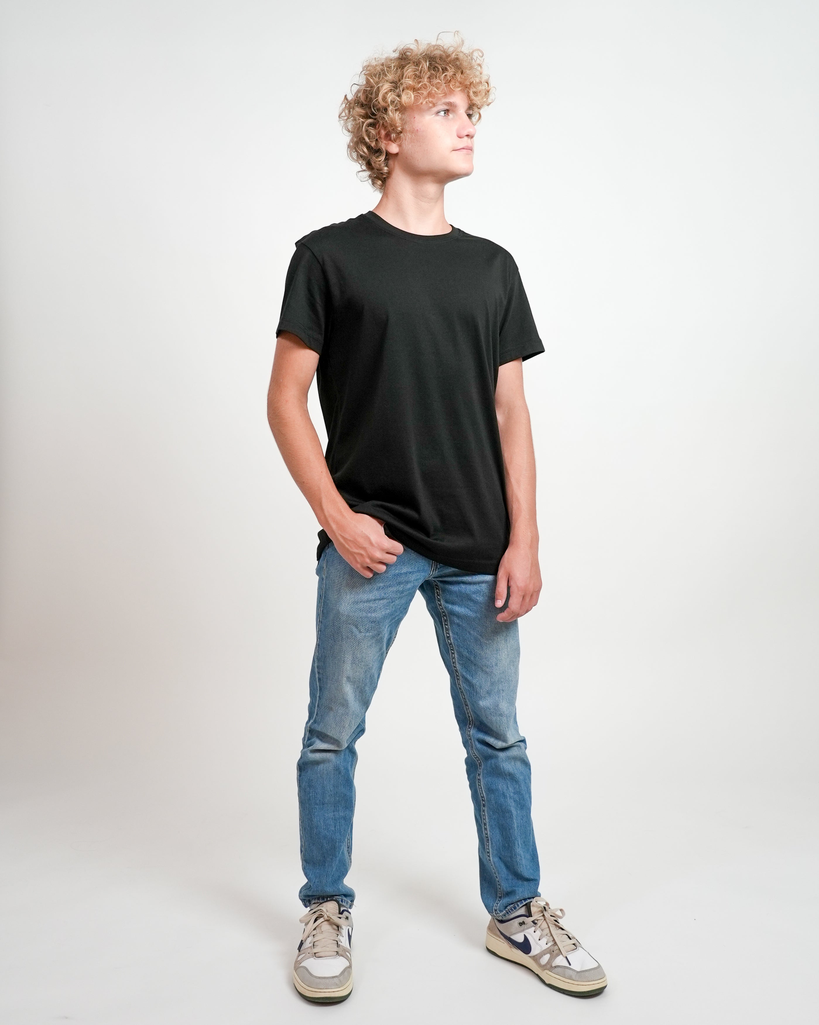 Male model wearing black t-shirt and jeans, standing in front of a white background.