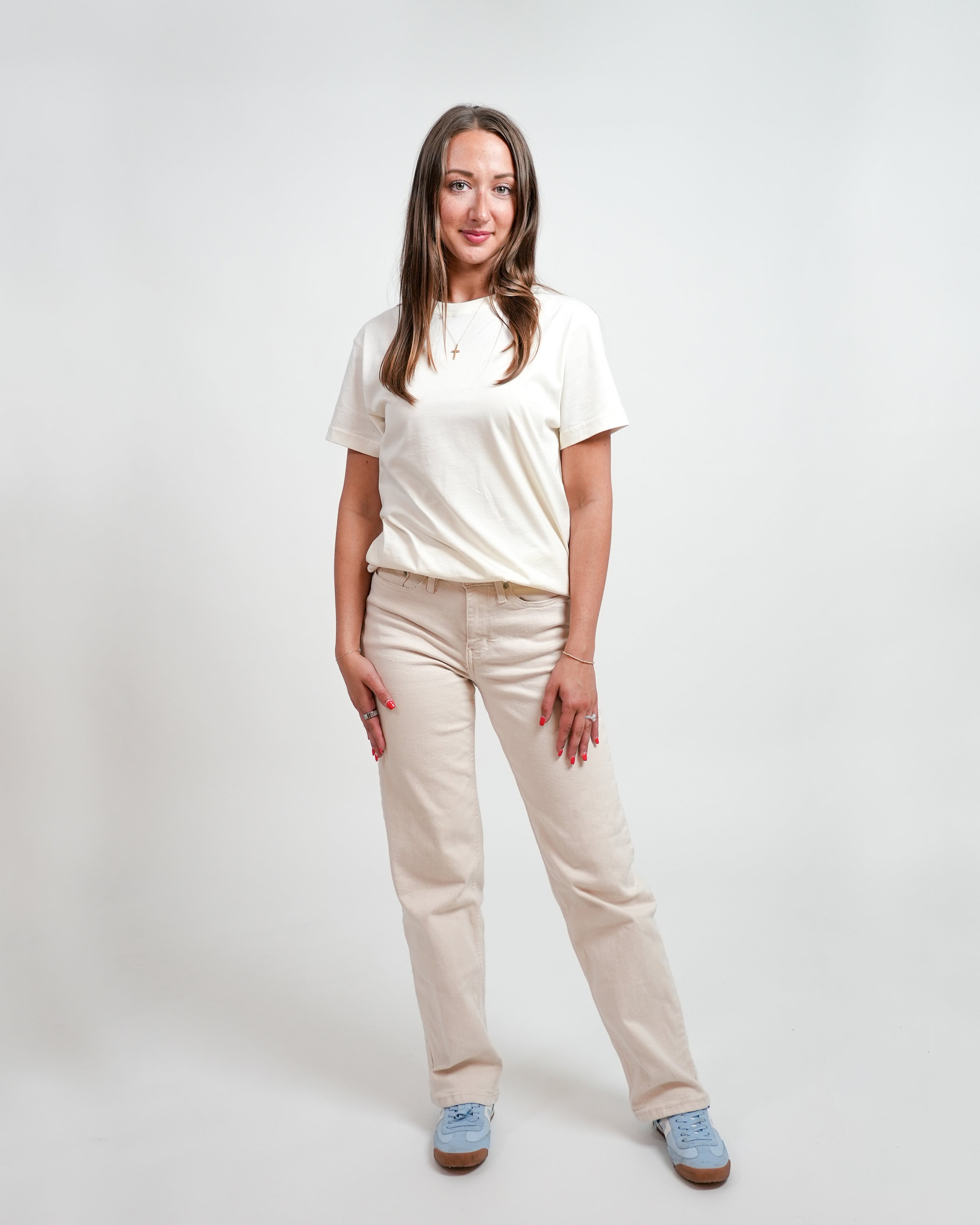 Female model wearing cream t-shirt and beige pants, standing in front of a white background.