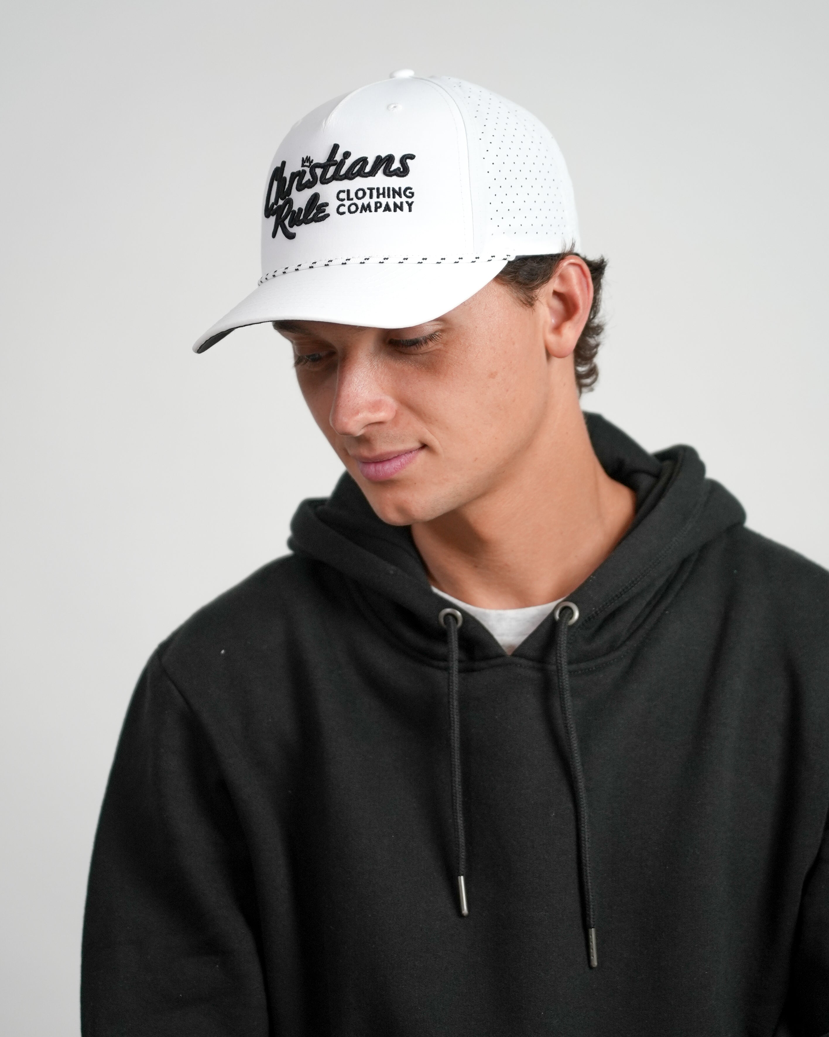 Male model wearing a white Christian golf rope cap with 'Christians Rule Clothing Company' embroidered text, standing against a white background.