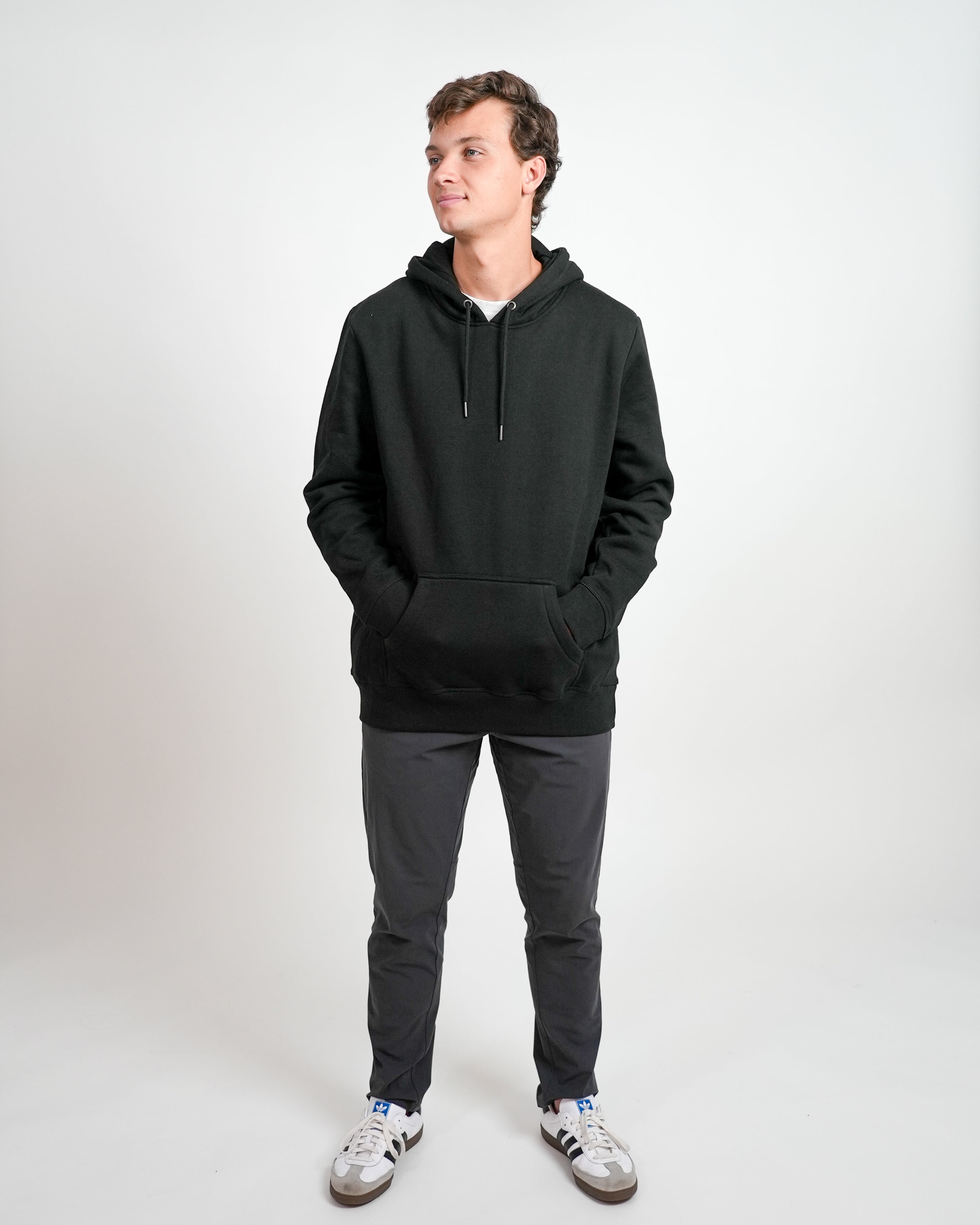 Smiling male model wearing black hoodie and gray pants standing against a white background.