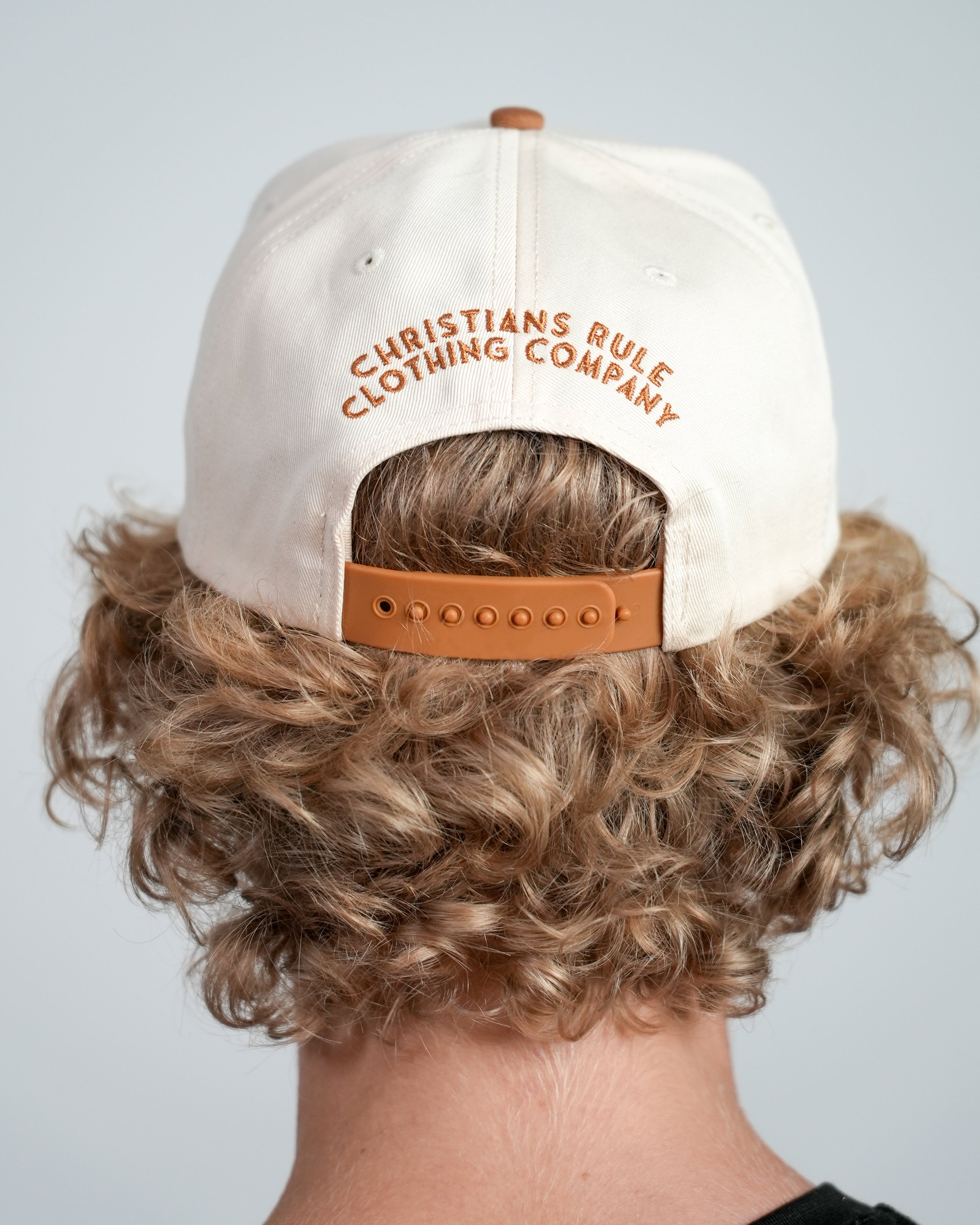 Male model wearing a cream Christian cap with 'Christians Rule Clothing Company' embroidered text, against a white background.