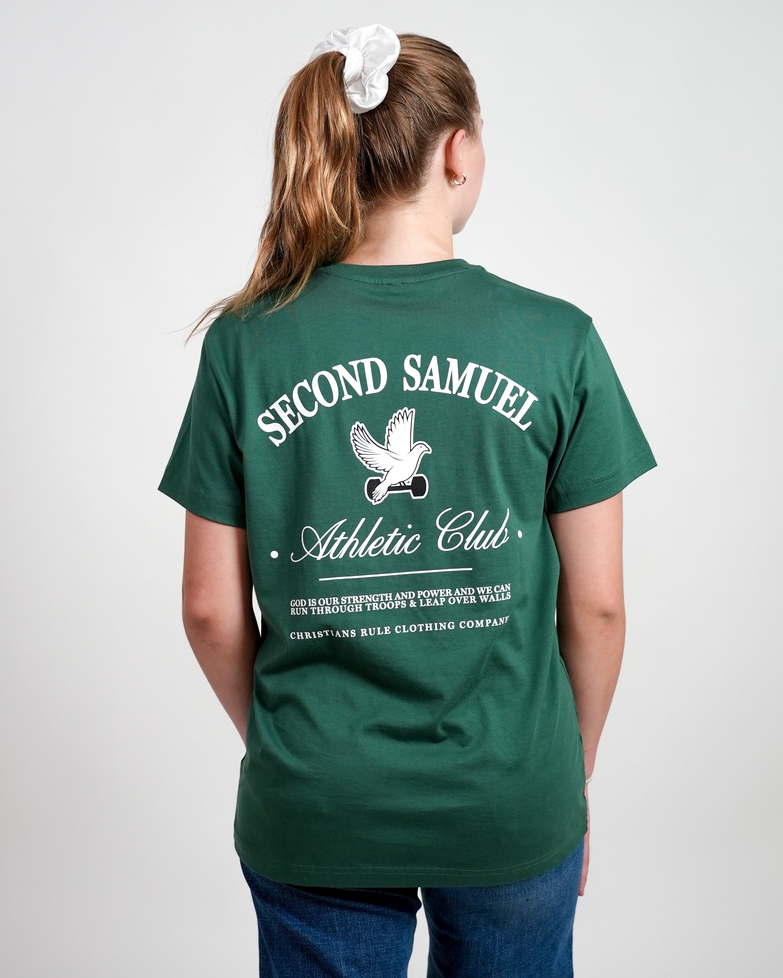 Female model wearing green Christian t-shirt with 'Second Samuel Athletic Club' text and graphic of dove holding a dumbbell; person stands against a white background.