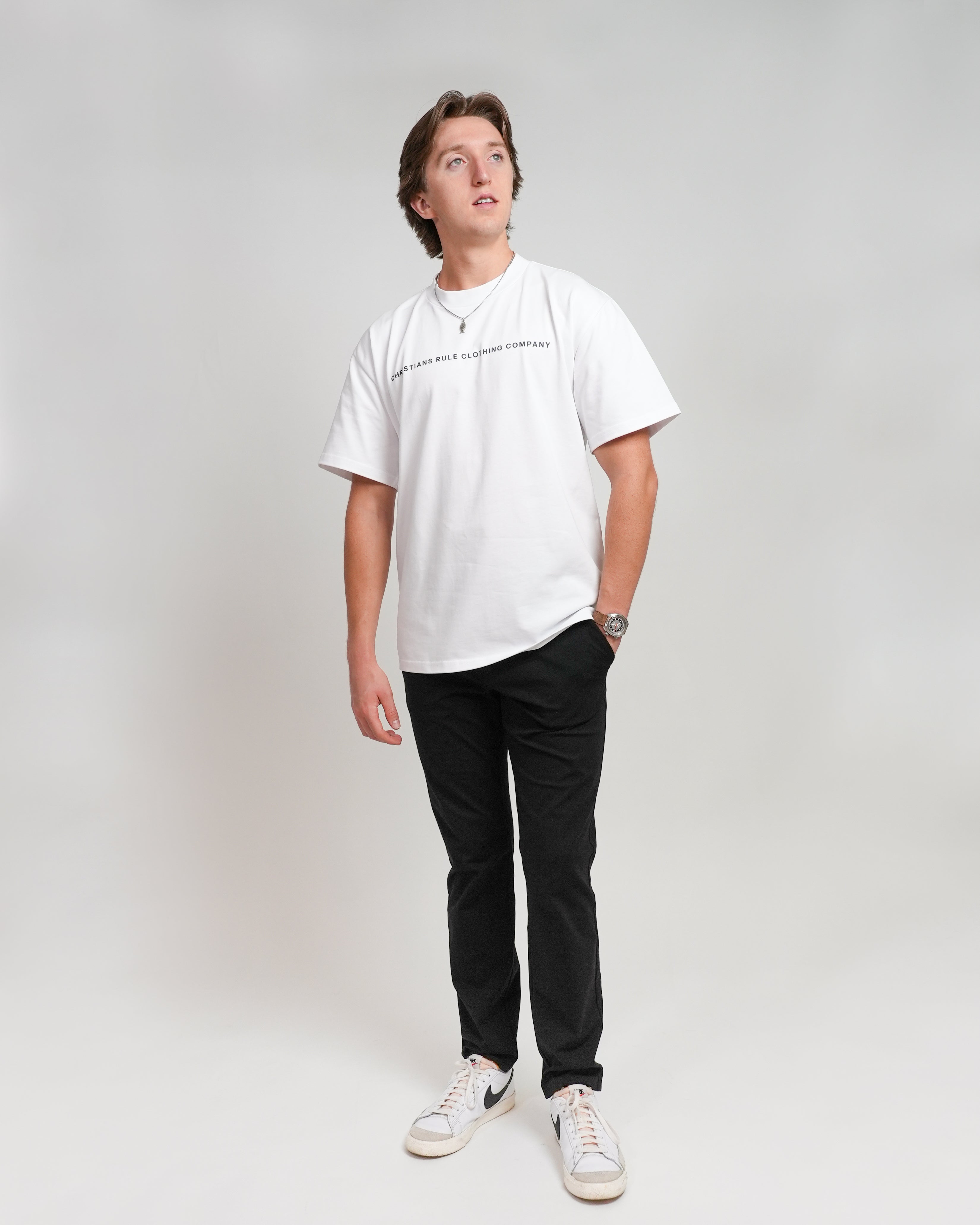 Male model wearing a white Christian heavyweight t-shirt with black text that says 'Christians Rule Clothing Company," standing against a white background.