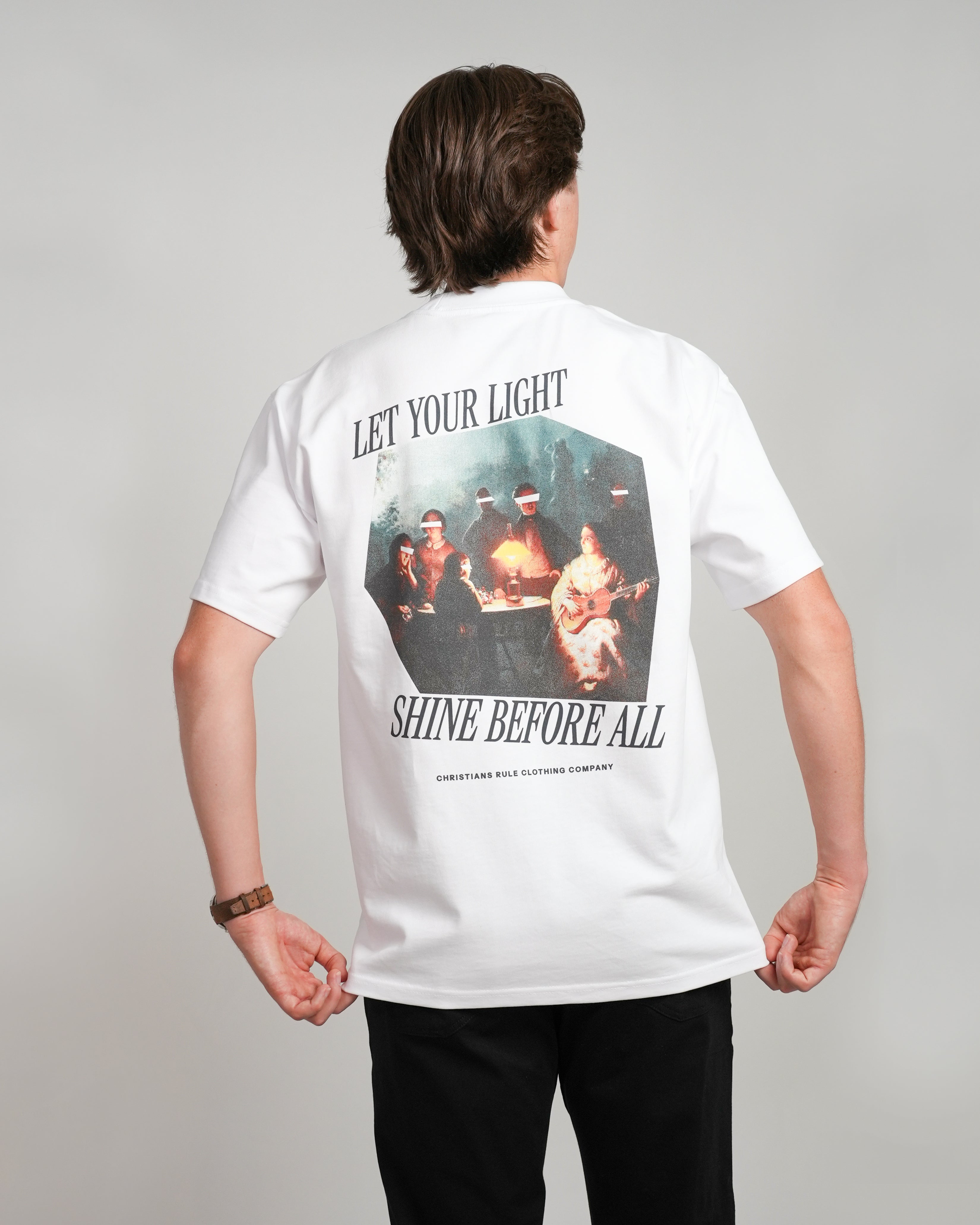 Male model wearing a white heavyweight Christian t-shirt with art design and black text that says 'Let your light shine before all', standing against a white background.