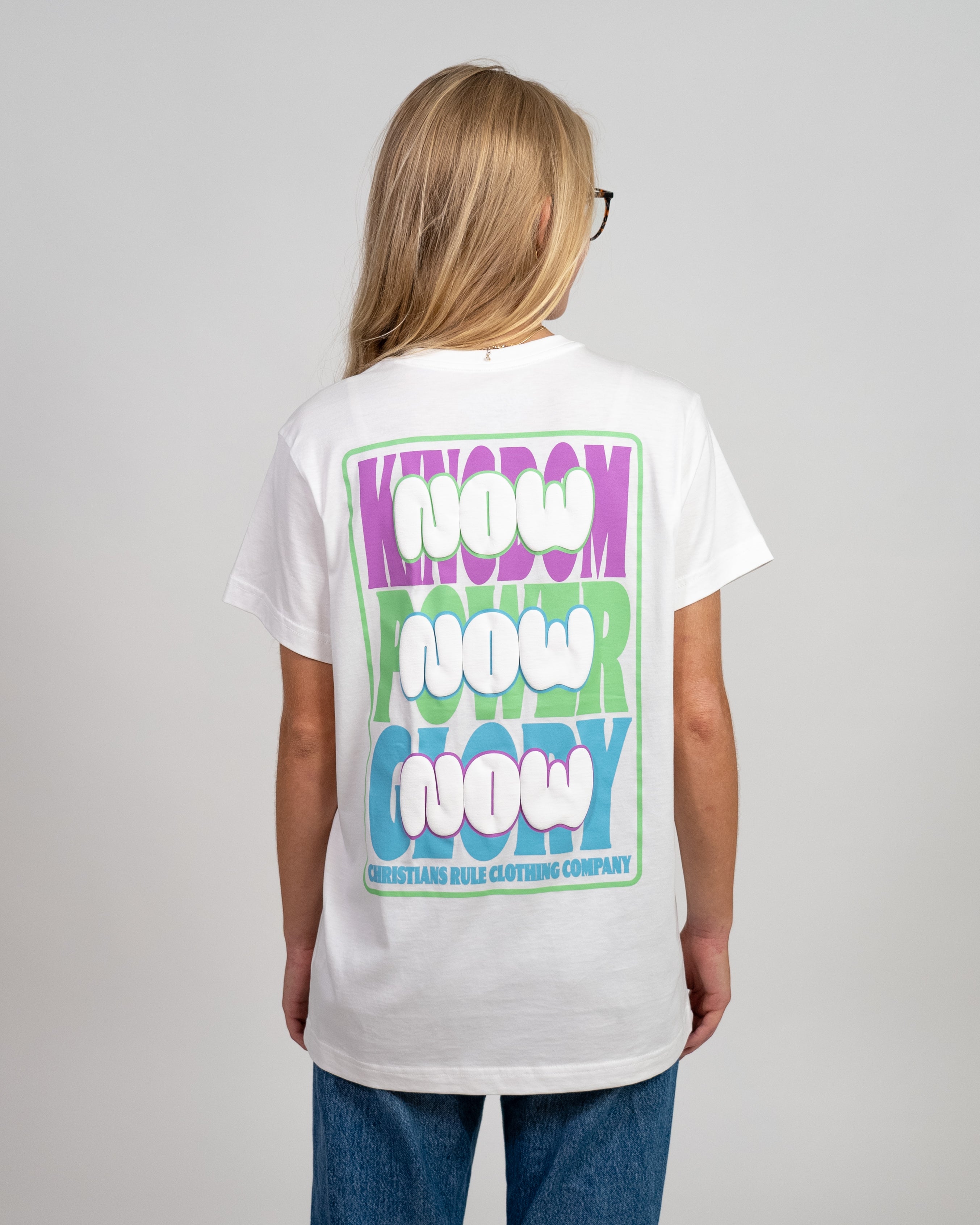 Female model wearing a white Christian t-shirt with colorful text graphic design, standing against a white background.
