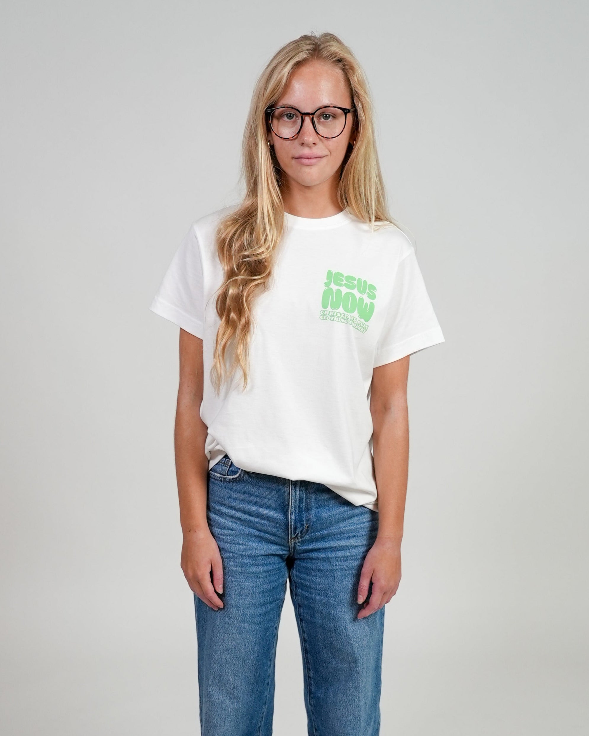 Female model wearing a white Christian t-shirt with "Jesus Now" graphic design, against a white background.