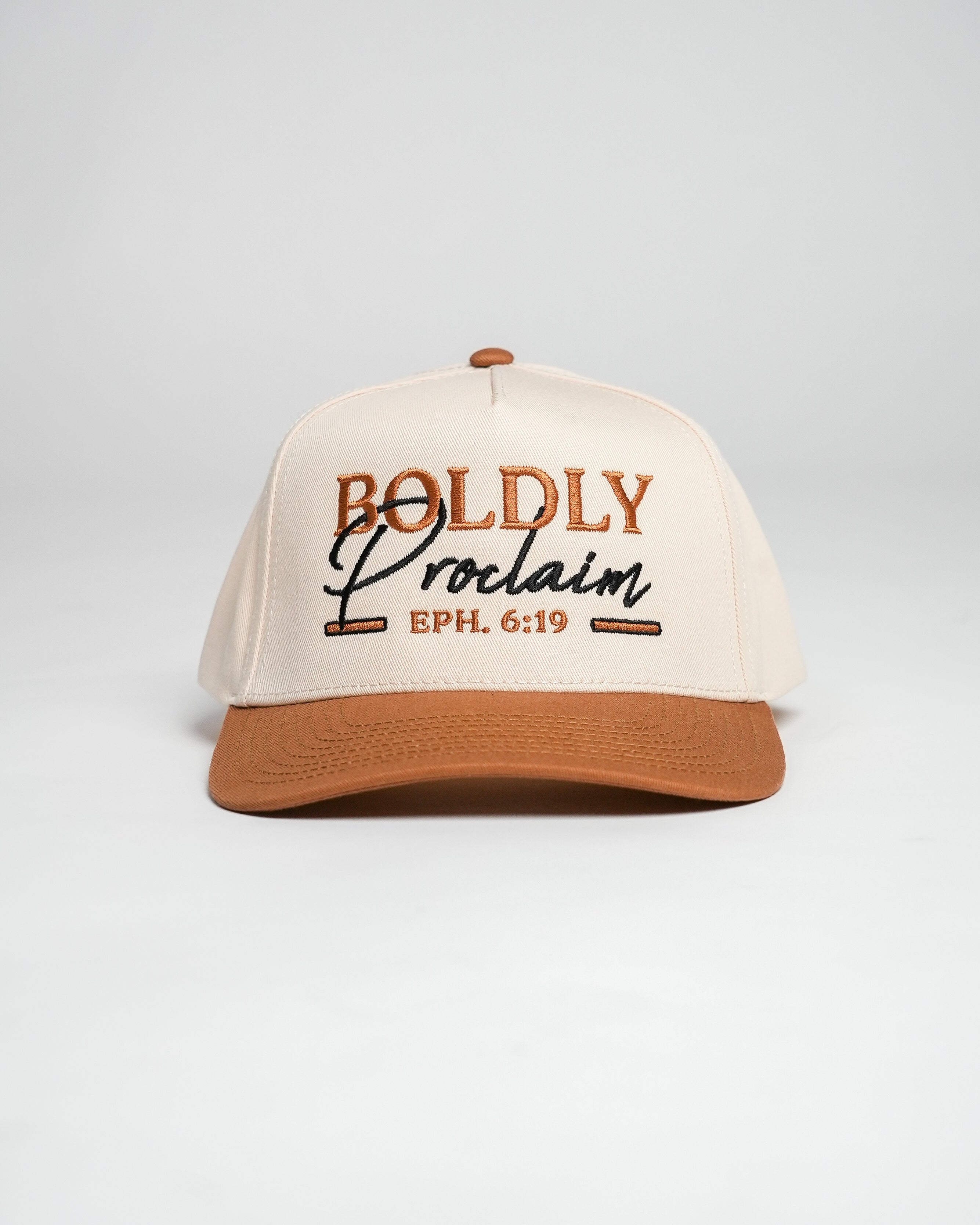 Cream and bronze Christian cap with 'Boldly Proclaim' embroidered text against a white background.