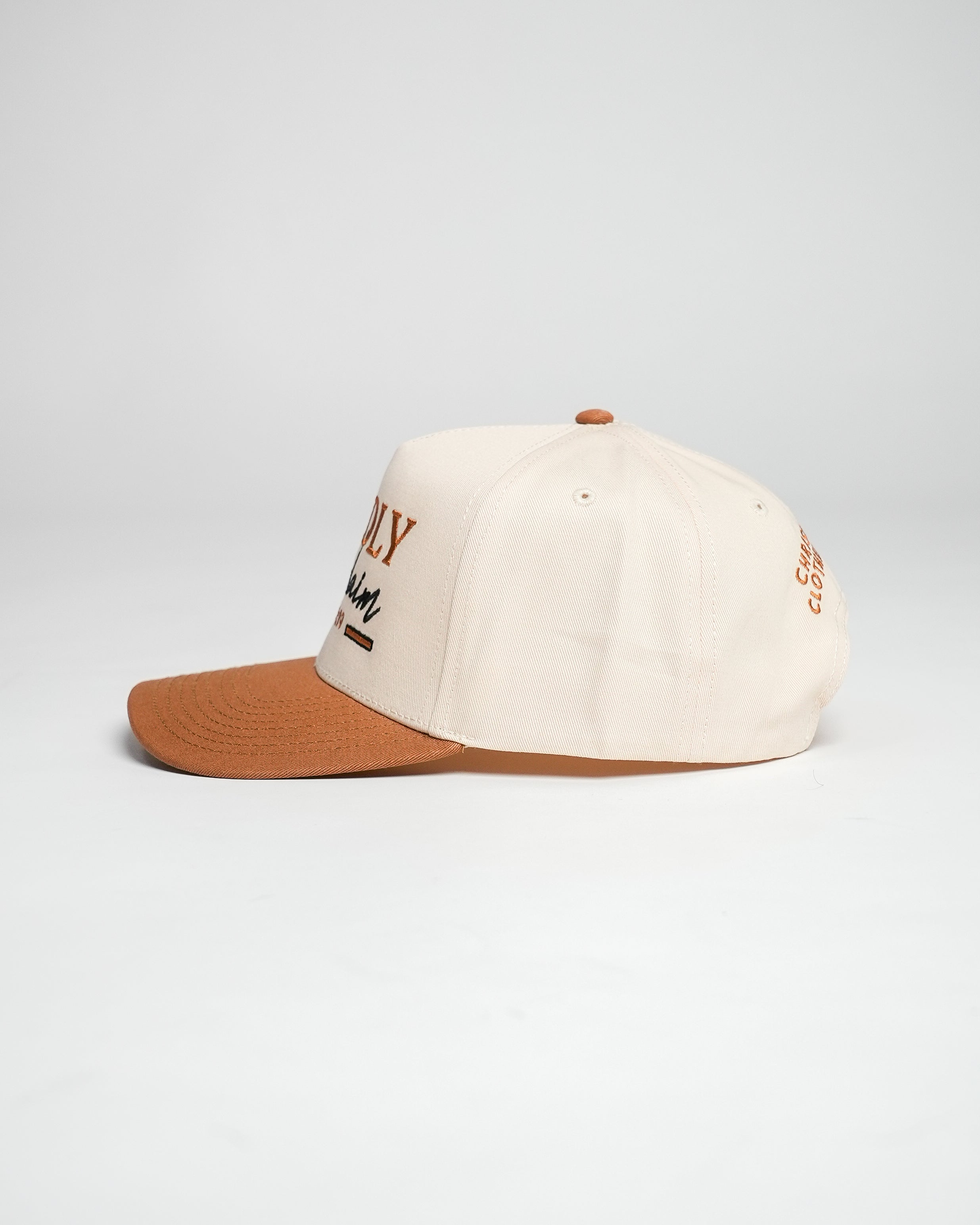 Side view of a cream and bronze Christian cap with embroidered text, against a white background.